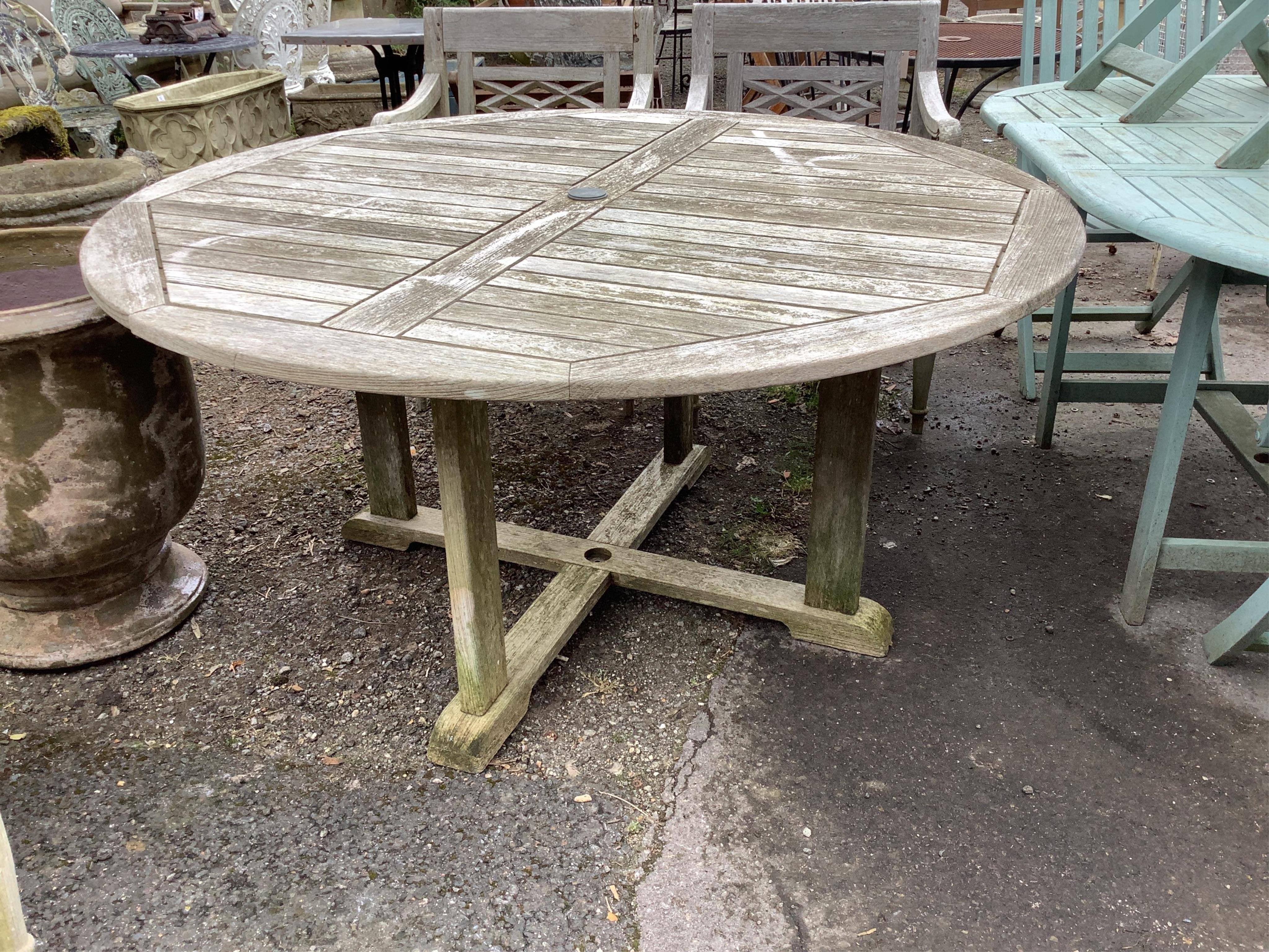 A circular weathered teak garden table, width diameter 150cm, height 73cm and four elbow chairs